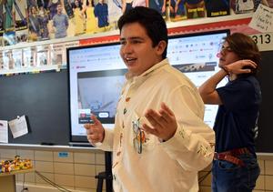 A student in a decorated shirt talks animatedly with another student in the background.