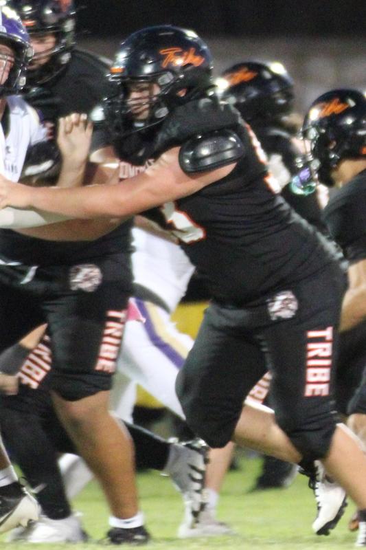 A football player in black uniform is blocking an opponent on the field.