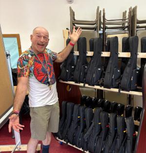 Enthusiastic teacher stands next to rack of new ukeleles