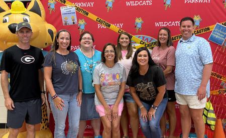 Group posing in front of a red wall with a wildcat mascot and caution tape.