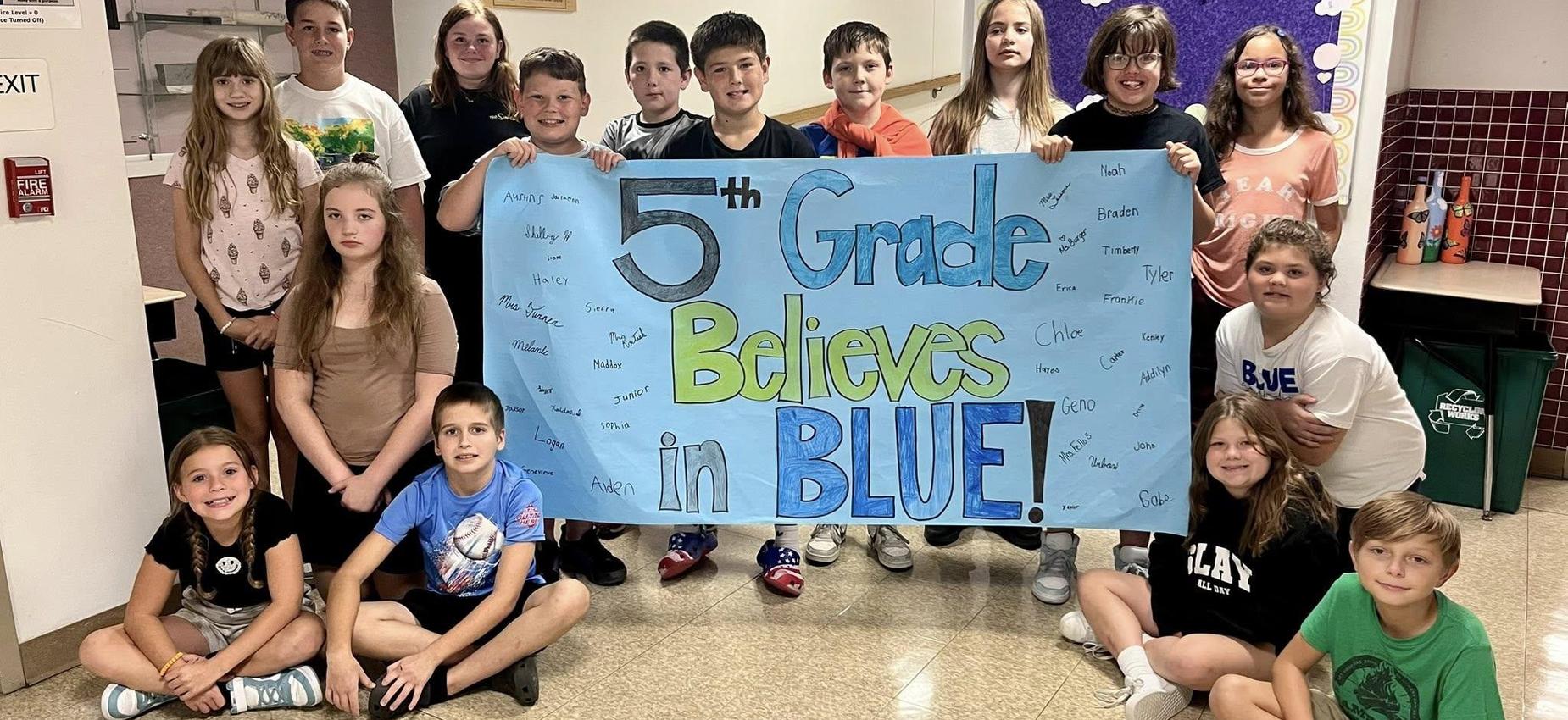 5th graders posing with their sign "5th Grade Believes in BLUE" for elementary night at the football game.