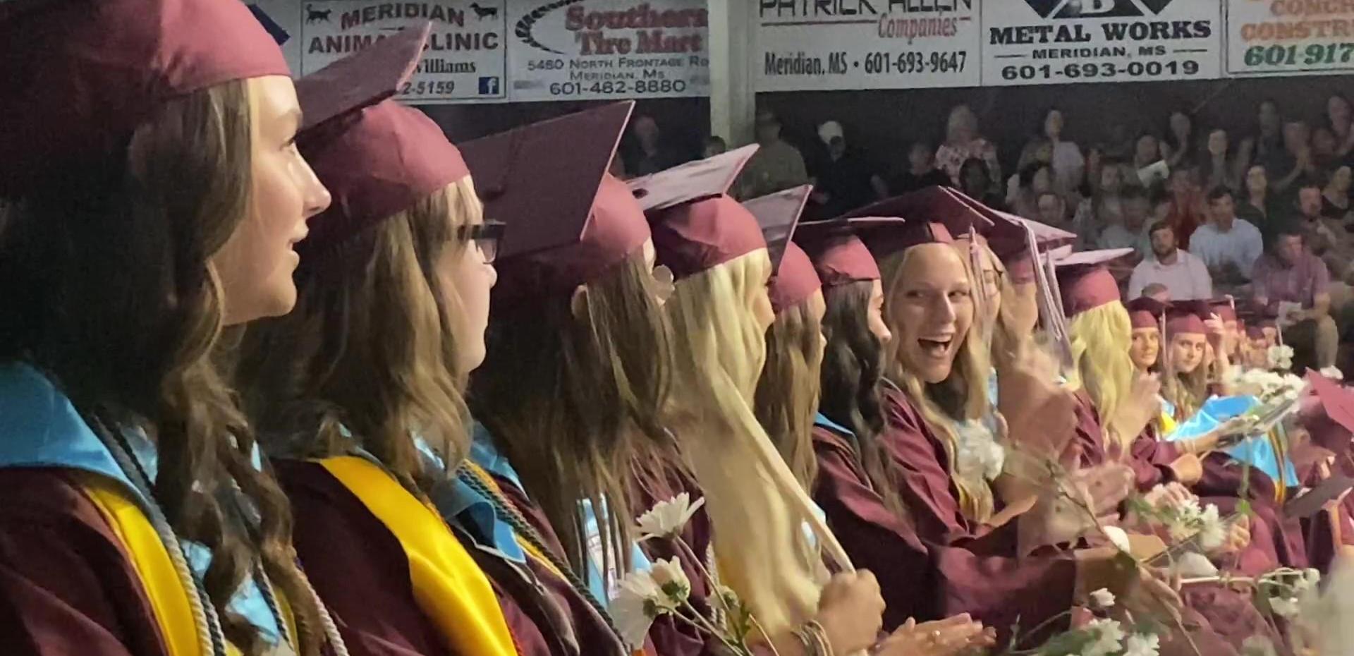 Graduates in caps and gowns celebrating at a ceremony with smiles and flowers.