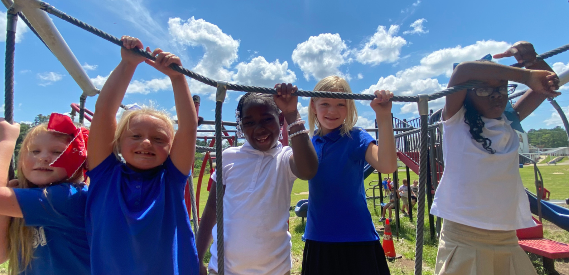 Five children smiling and playing on a playground structure outdoors.