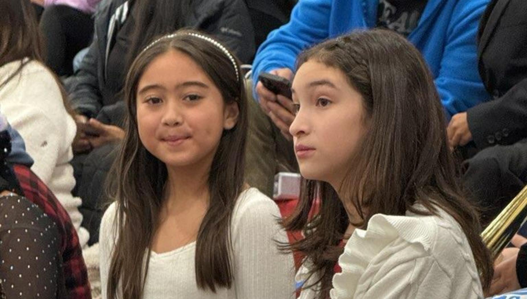 Two young girls sitting together, one smiling and the other looking thoughtful.