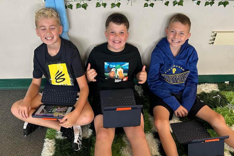 three students sit on the floor holding their iPads
