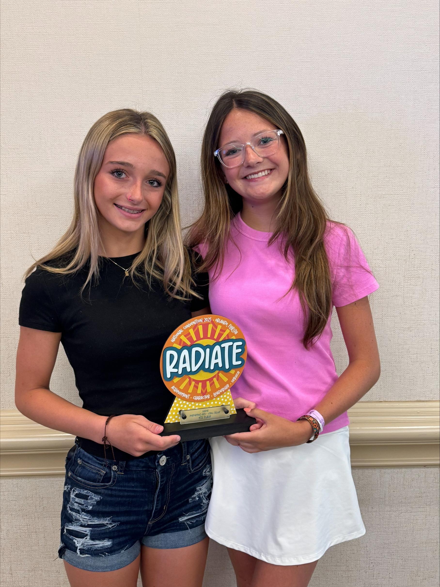 Two girls holding a Radiate trophy. 