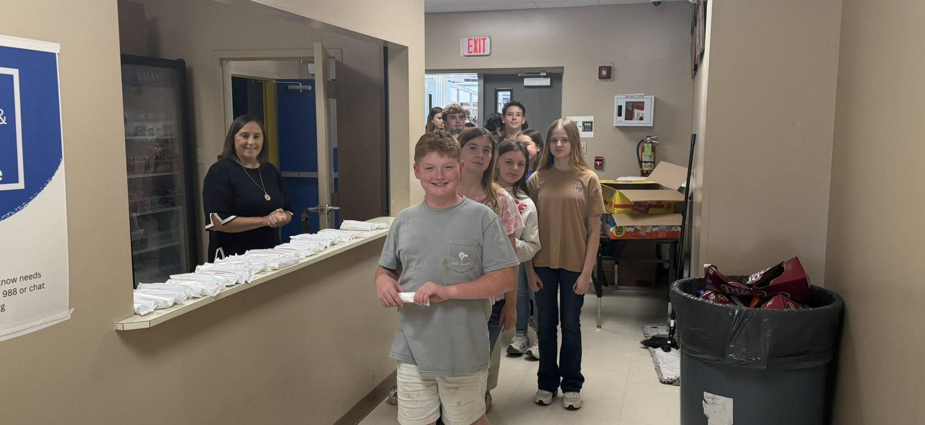 Students line up for lunch in a hallway with a teacher supervising.