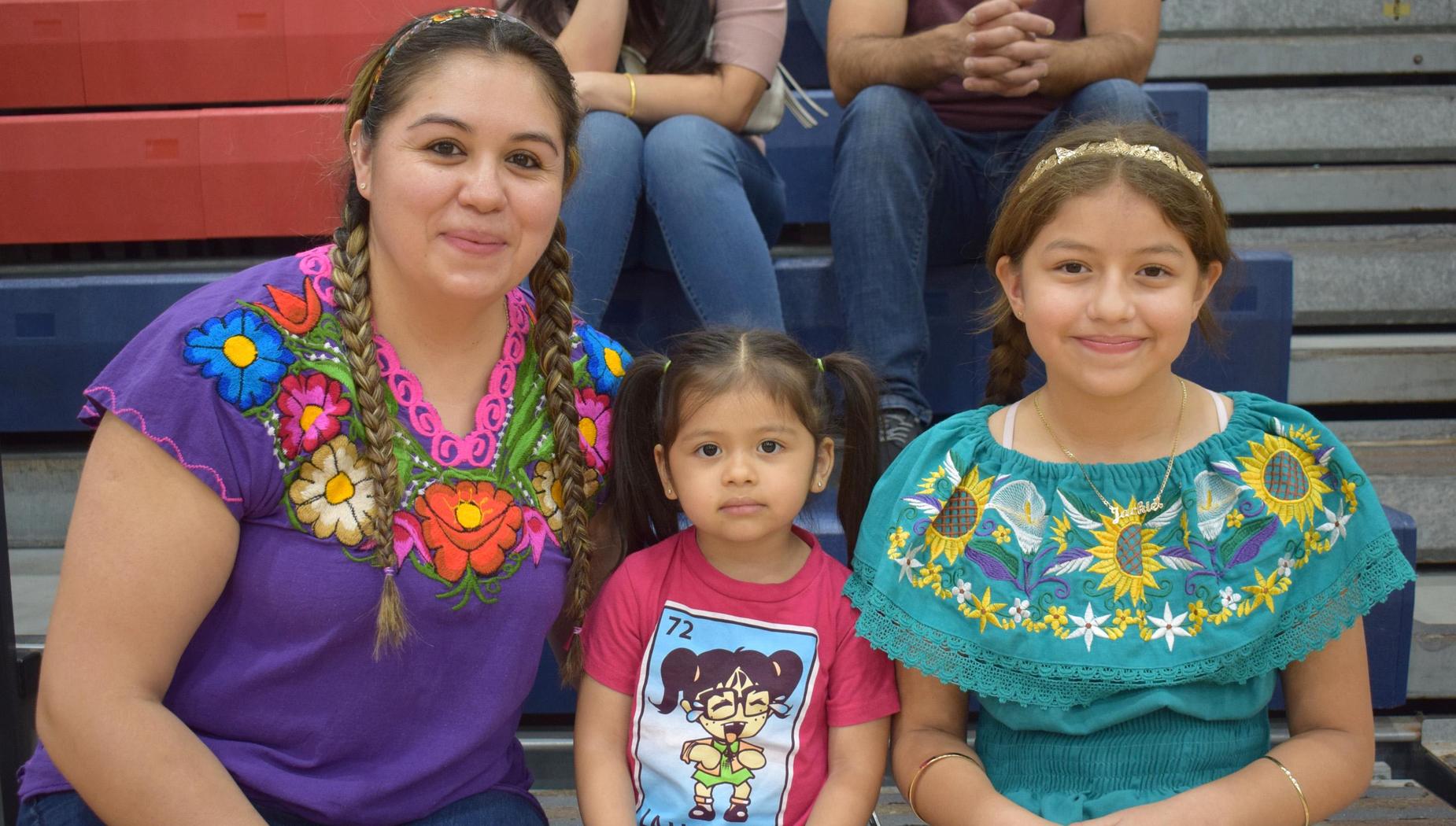 A woman and two girls in traditional Mexican attire, smiling for the camera.