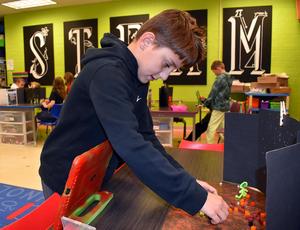 A boy focuses on his project, arranging materials on a science-themed table.
