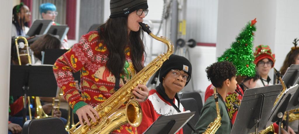 student in Christmas sweater soloes on the saxophone