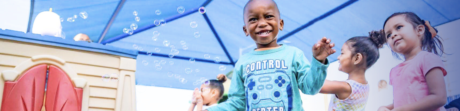 A young boy stands proudly in front of a colorful playhouse, smiling and ready for playtime adventures.