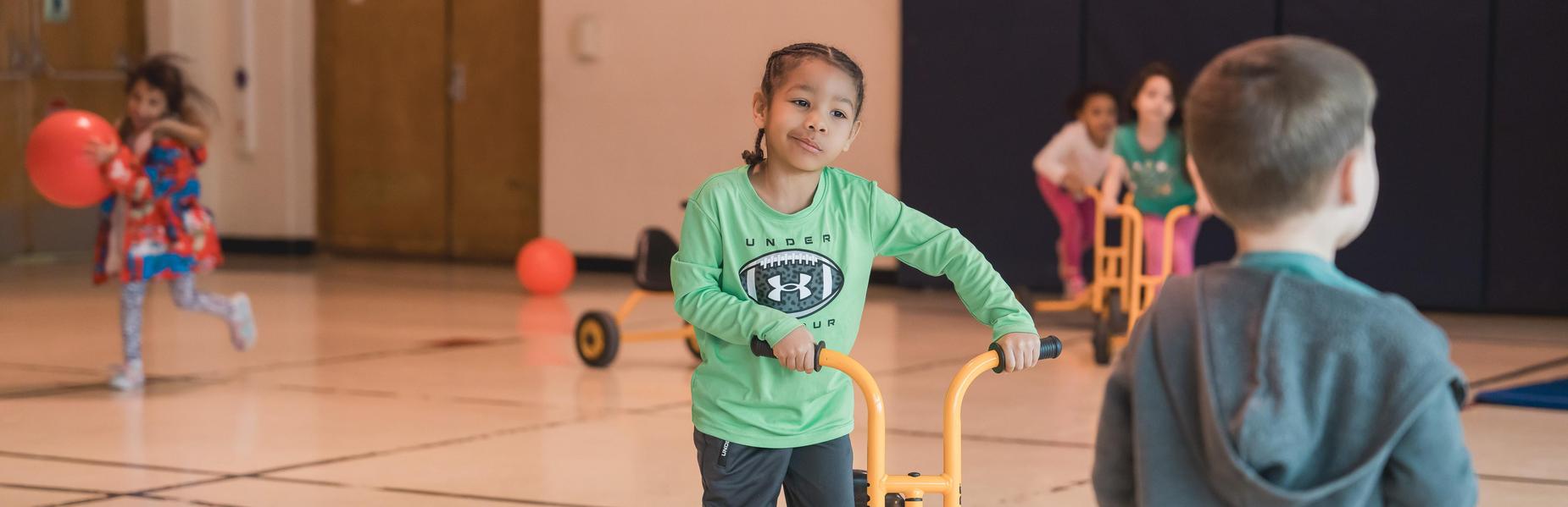 Children engage in play with tricycles in a gymnasium.