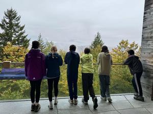 Five individuals standing together, gazing at a scenic view of trees and mountains.