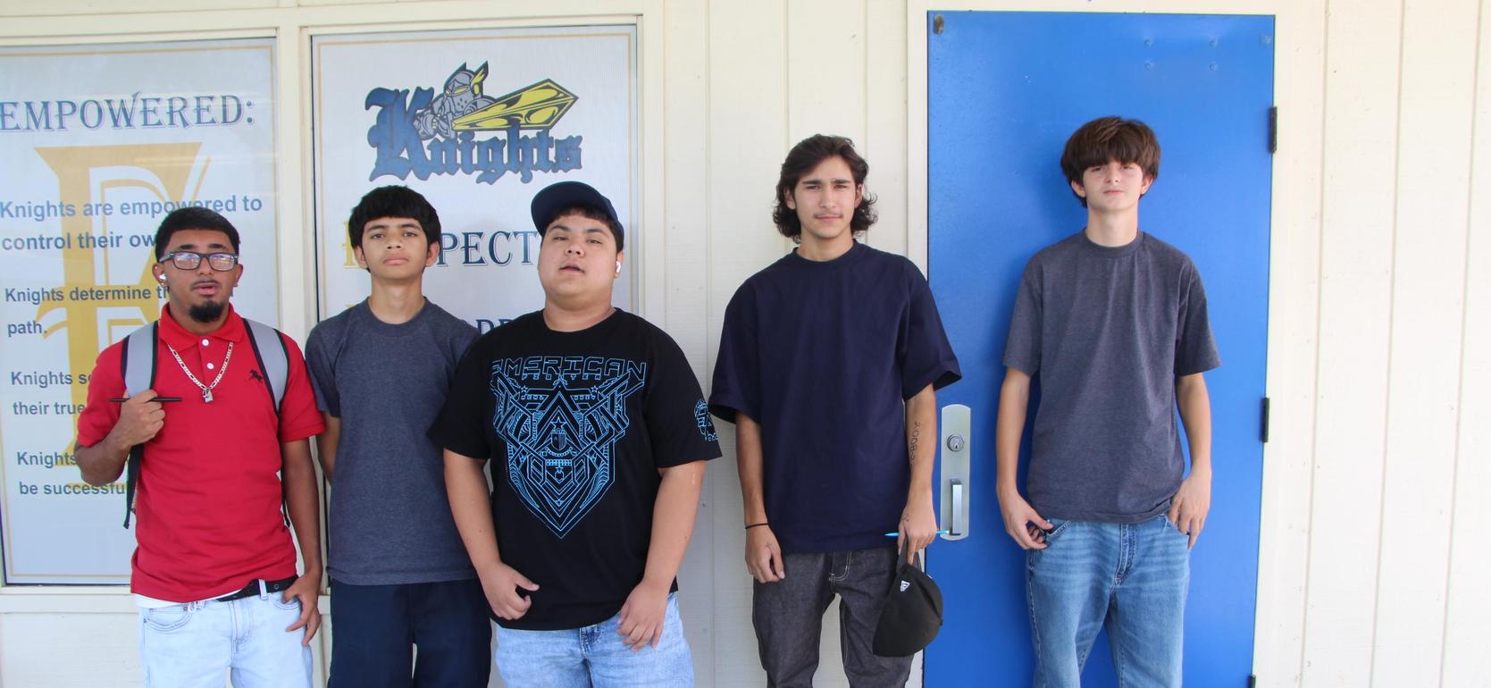 Five young men standing in front of a blue door, wearing casual clothing.