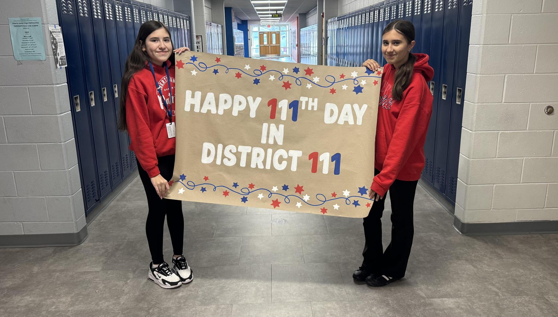 Two students in red hoodies holding a celebratory banner for District 111's 111th day.