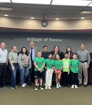 A group photo of people, including children and officials, in a meeting room.