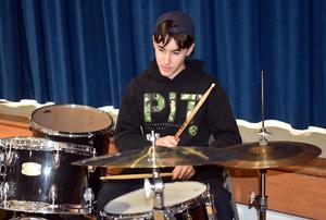 A young drummer playing a drum set with focused expression.