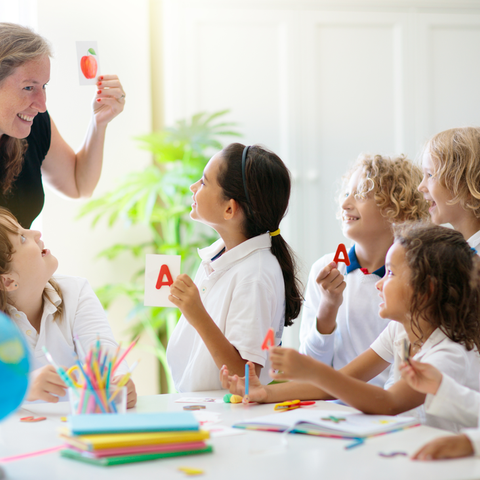 A teacher showing flashcards to engaged children in a bright classroom.