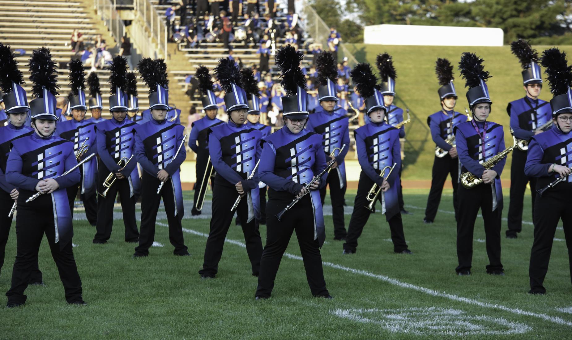 Marching band members in blue and black uniforms standing on a field.