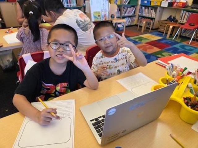 Two children smiling and posing with peace signs in a classroom setting.