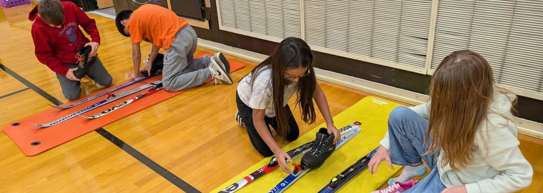 Students assembling skis on mats in a gymnasium.