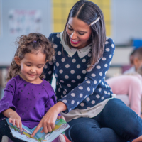 Teacher sitting on floor reading to young child