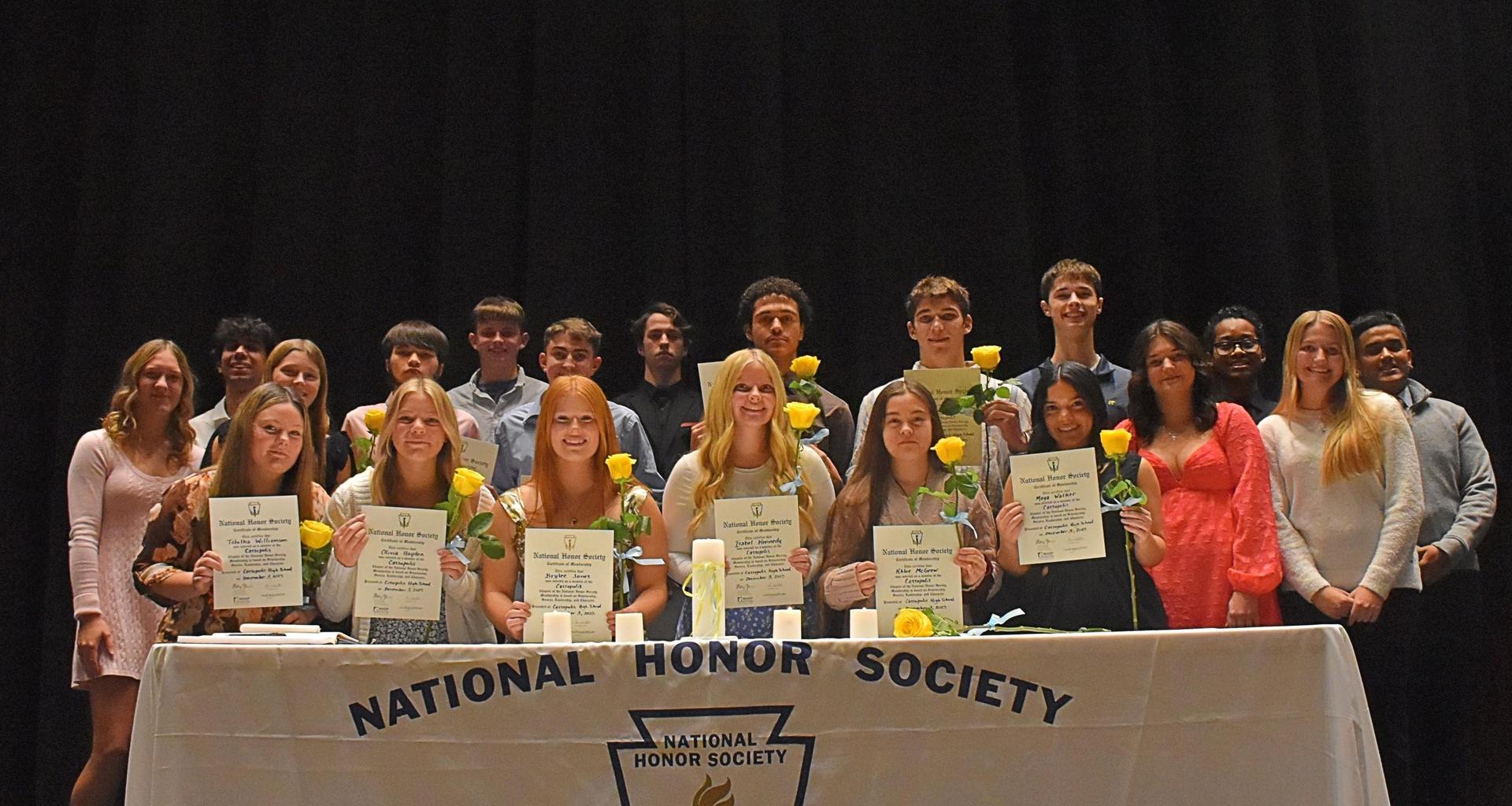 A group of students holding certificates and yellow roses at a National Honor Society ceremony.