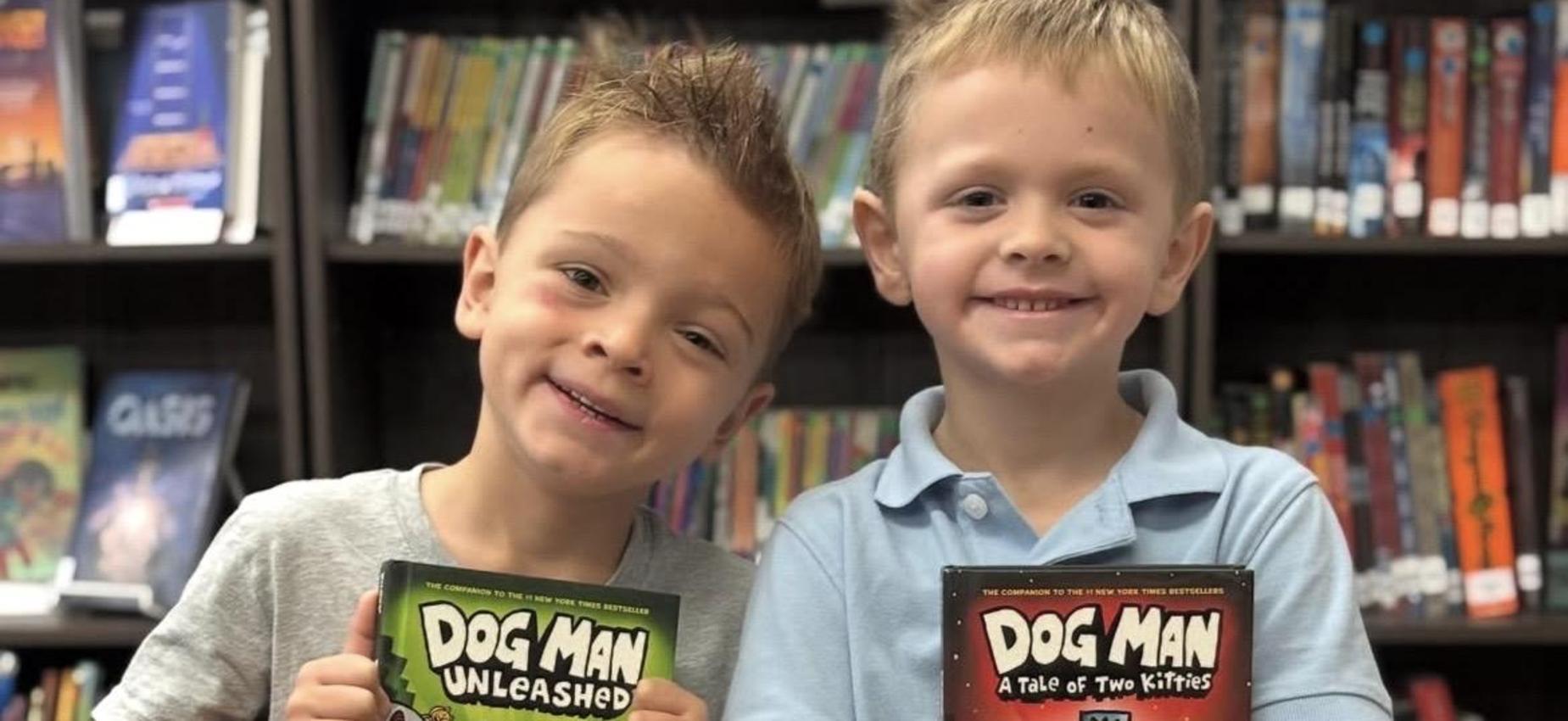 Two children holding 'Dog Man' books in a library setting.