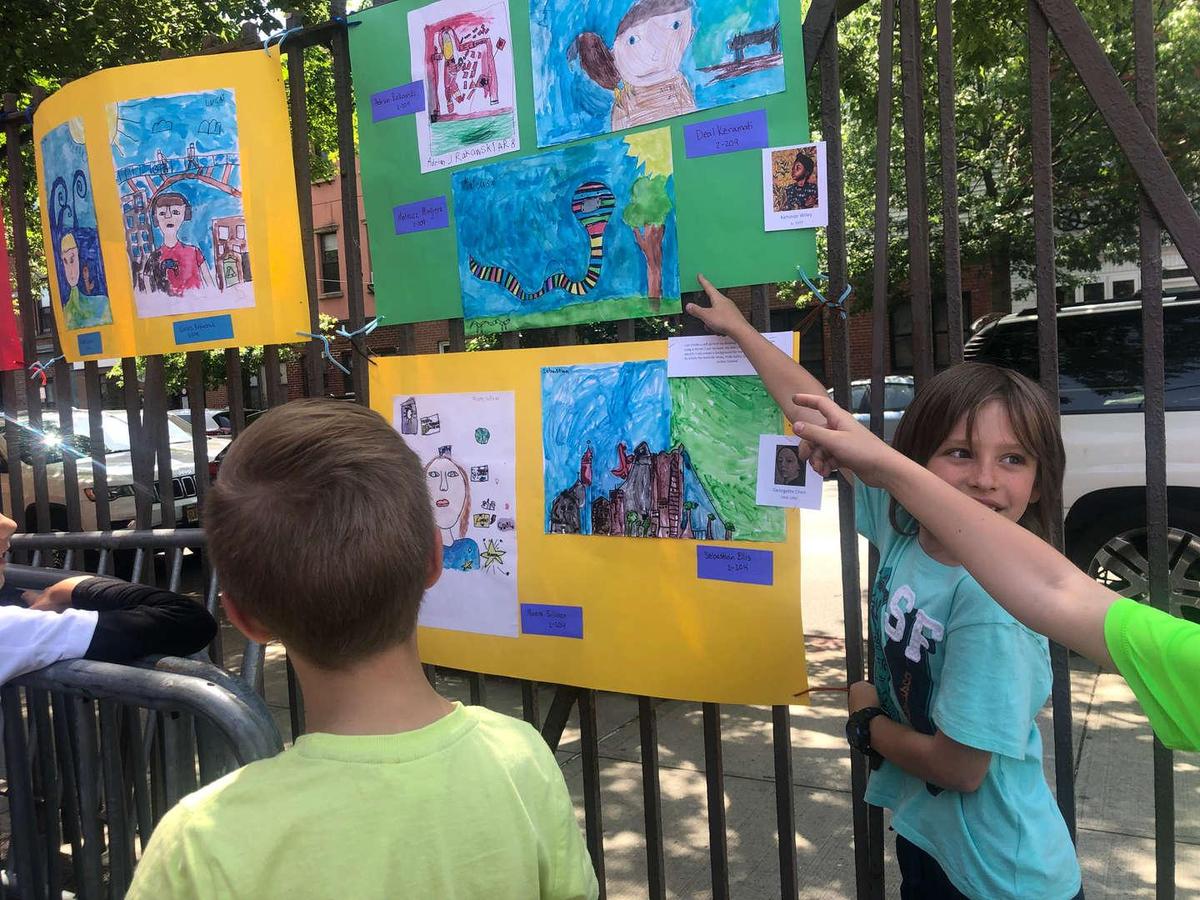Children admiring colorful artwork displayed on a fence.