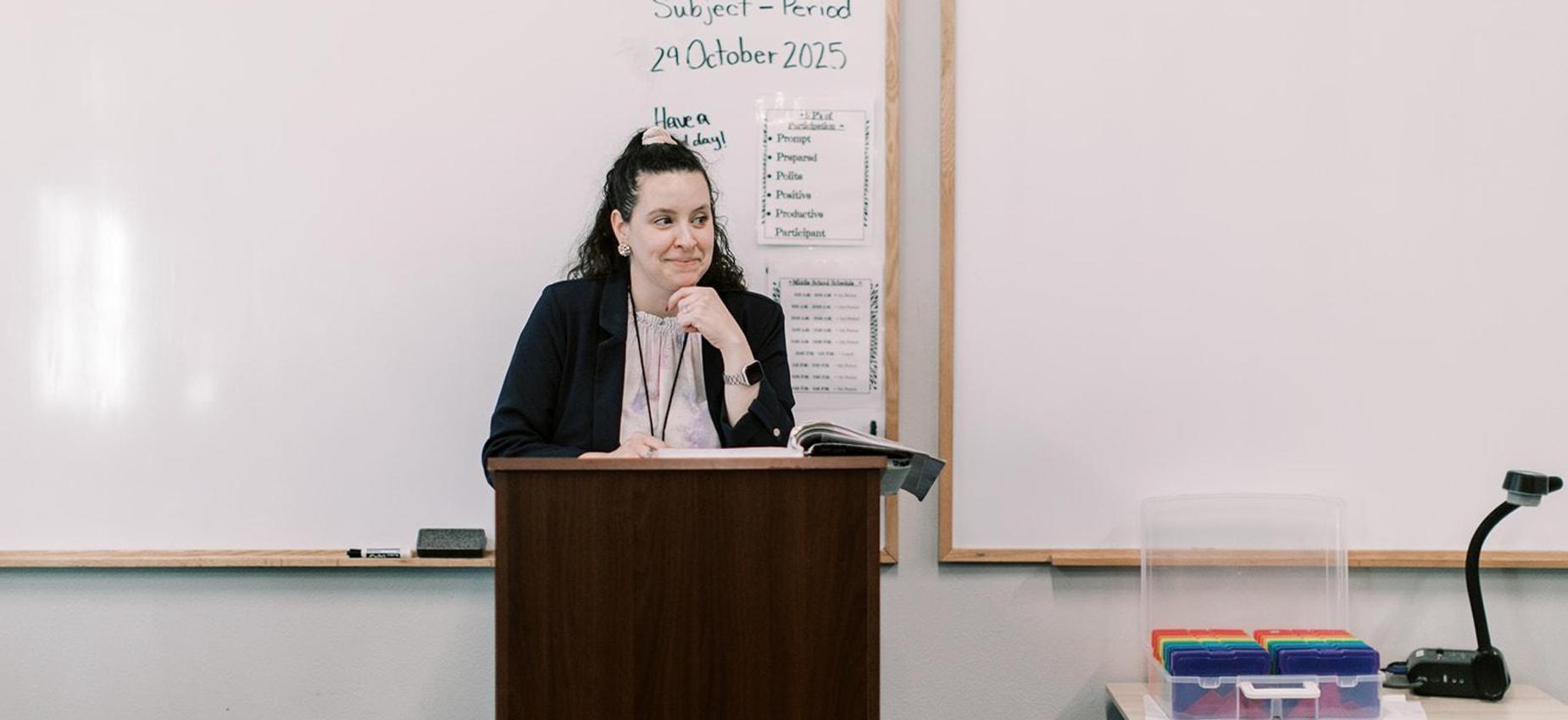 Teacher speaks from a podium at the front of the classroom