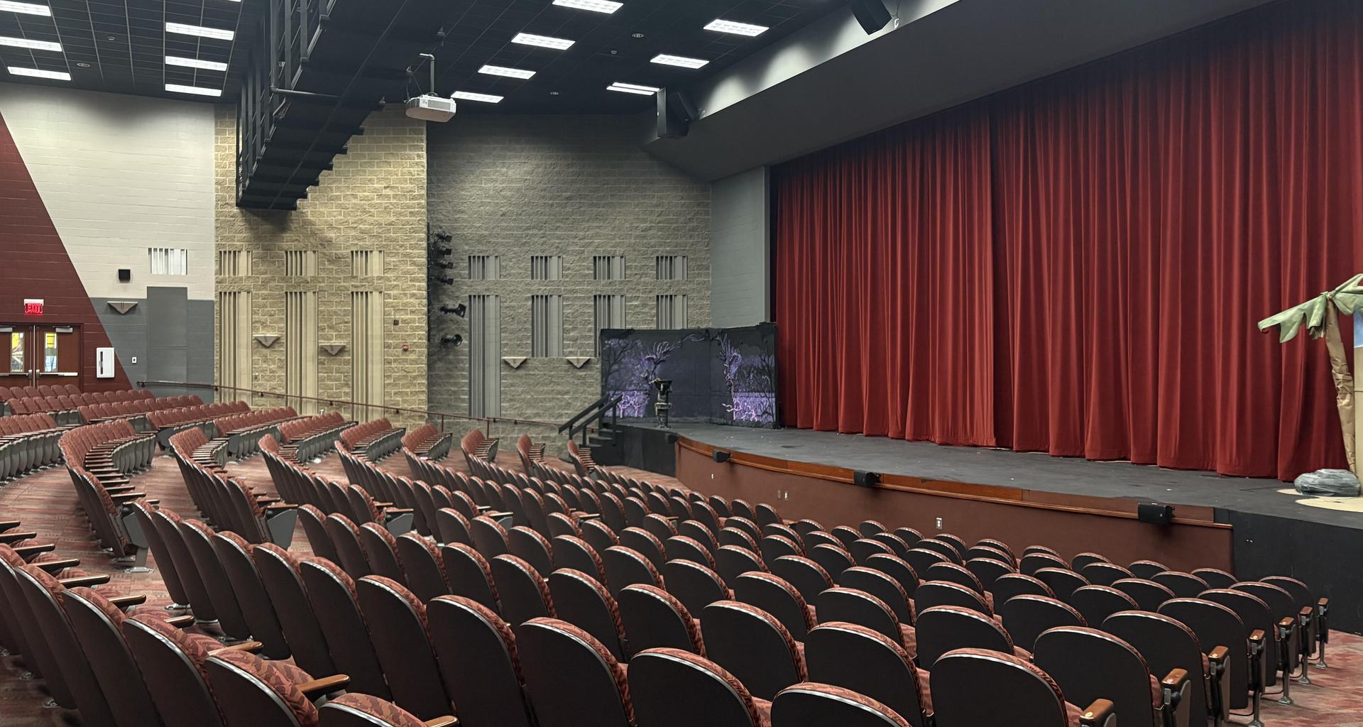 An empty theater interior with red curtains, rows of seats, and a stage.