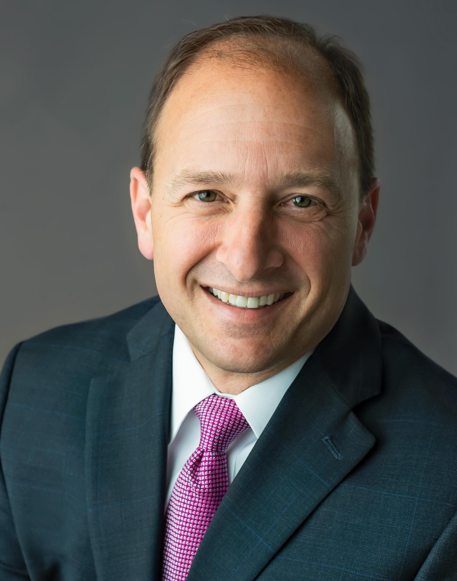 smiling white man, balding with brown hair, in a blue jacket, pink tie