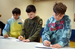 three boys writing on pieces of paper