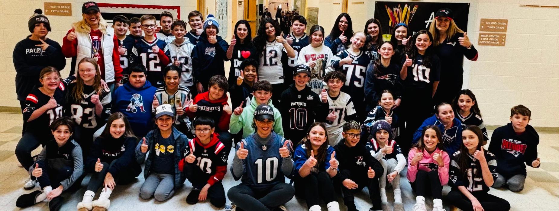 Staff and students shown together in a large group, wearing football jerseys and giving a "thumbs up" for spirit day before the Super Bowl.