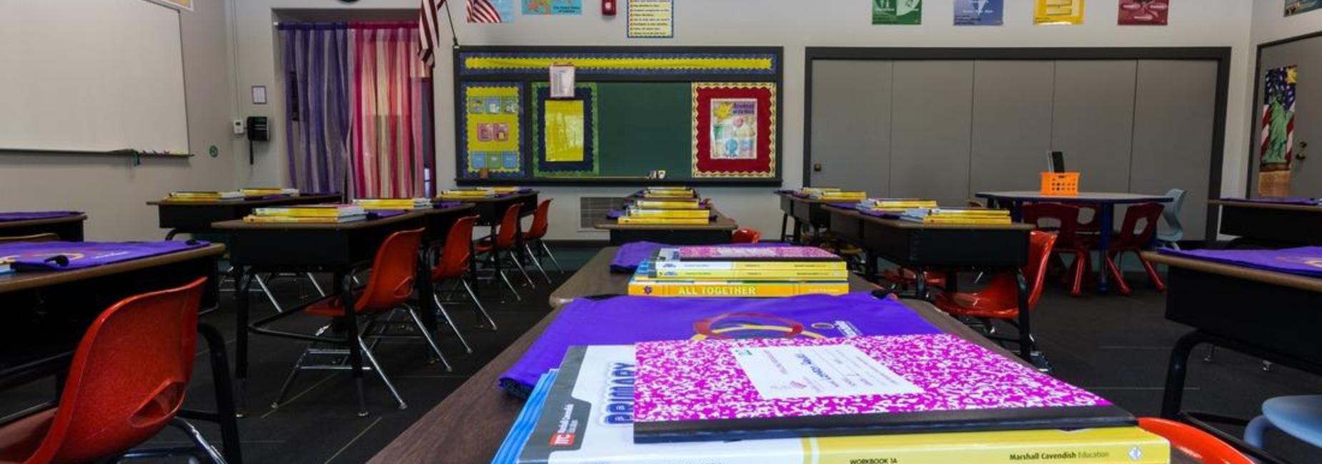 An empty classroom is pictured with notebooks stacked on desks