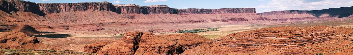 Hikers exploring a rugged, red desert landscape with distant mesas and hills.