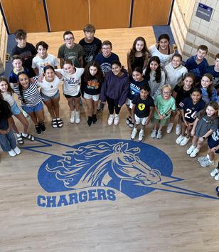 A group of students posing in a gym with a blue horse logo on the floor.