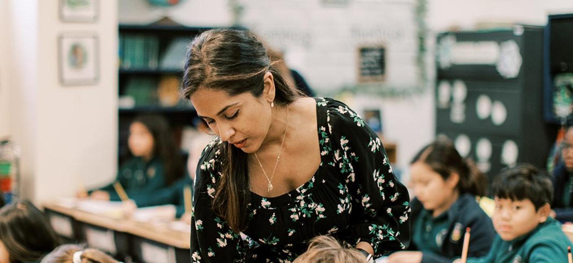 Teacher smiles while helping elementary students with their work