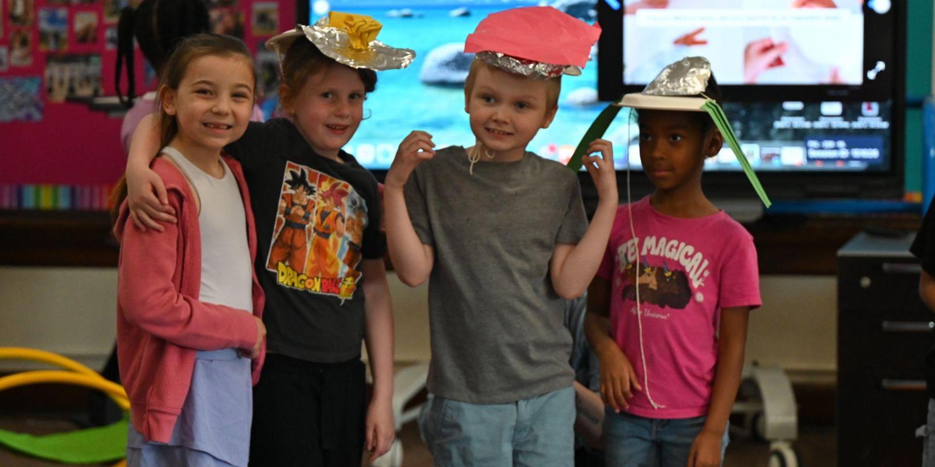 Four children wearing creative hats pose together happily.