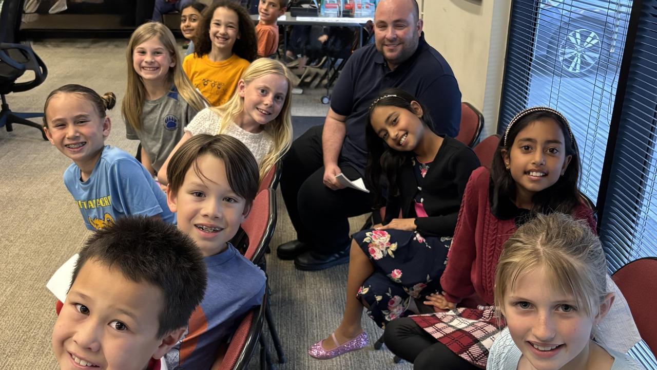 A group of smiling children and an adult sitting together in a classroom.