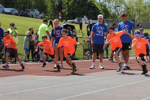 Penn Yan student-athletes in orange shirts run on the track as student volunteers cheer.