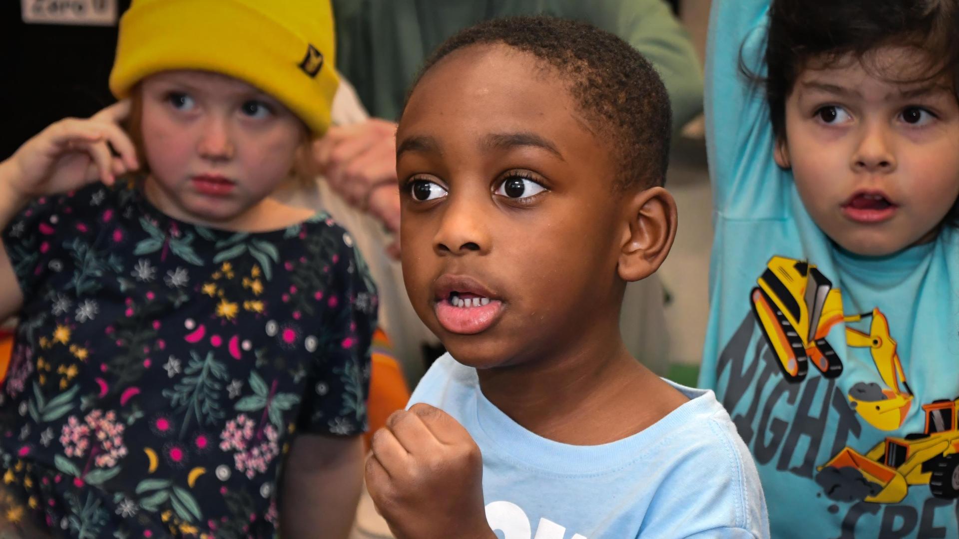 A young boy looks surprised while surrounded by other children at an event.