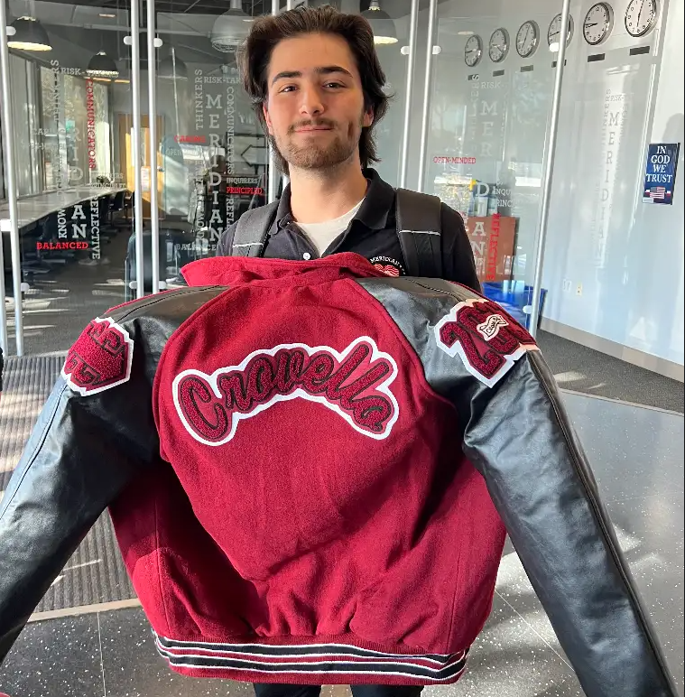 A student holds up his red and black letter jacket