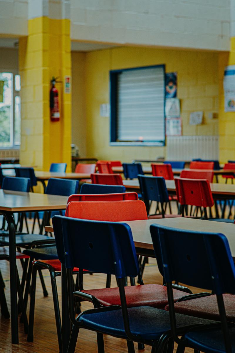 School Cafeteria with empty tables and red and blue chairs arranged in rows.