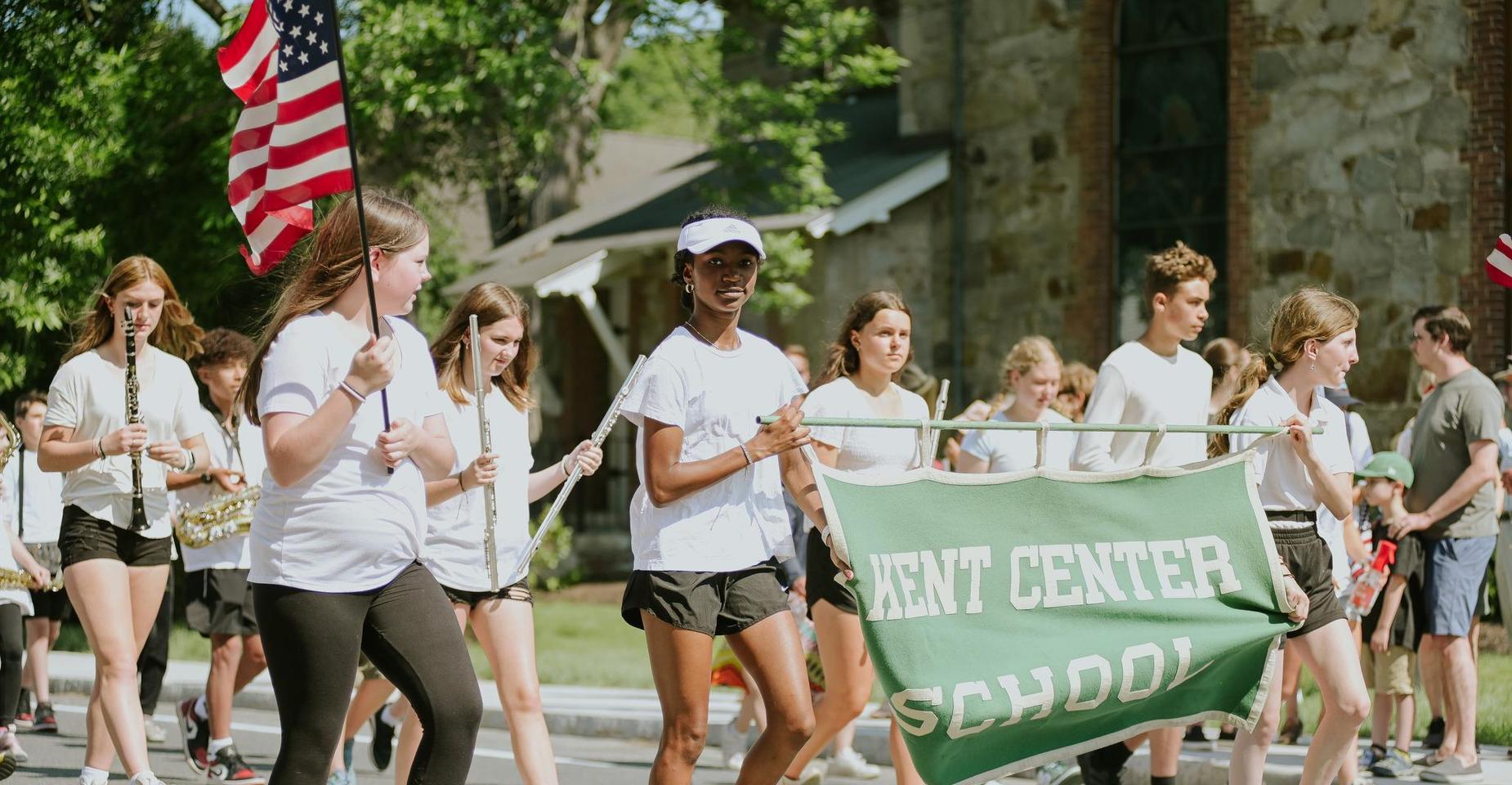 Marching group of students carrying a banner for Kent Center School in a parade.