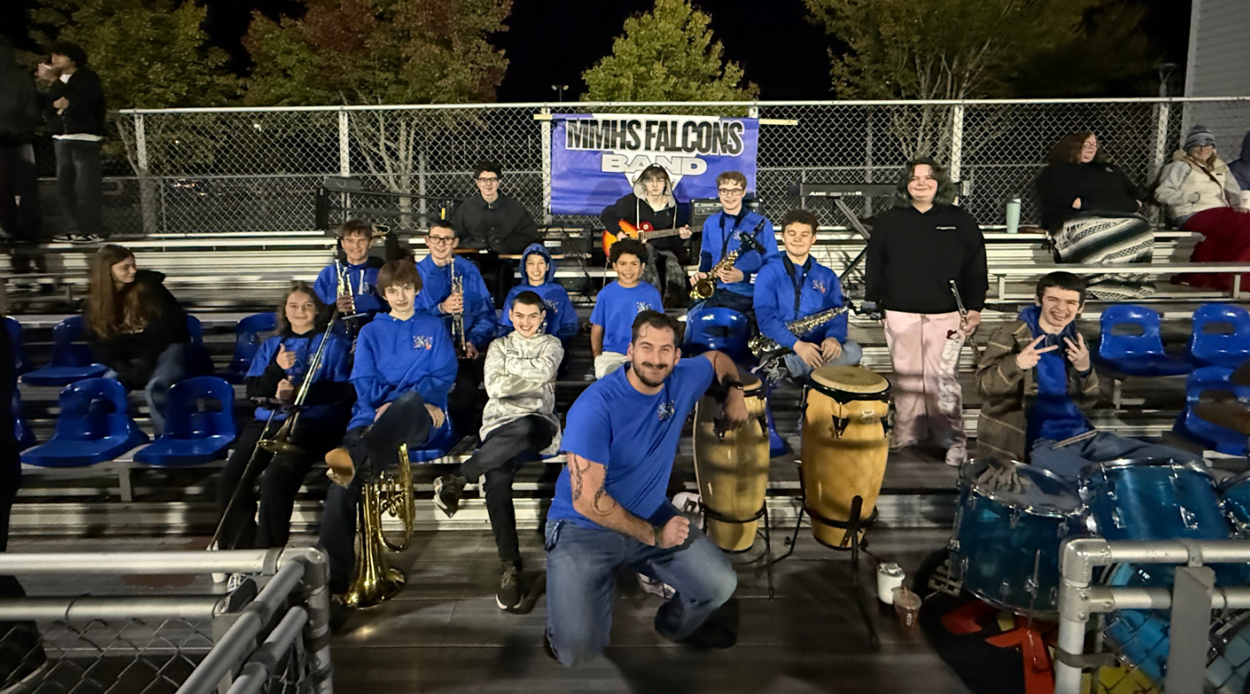 Student band poses together in blue shirts at a sports event.
