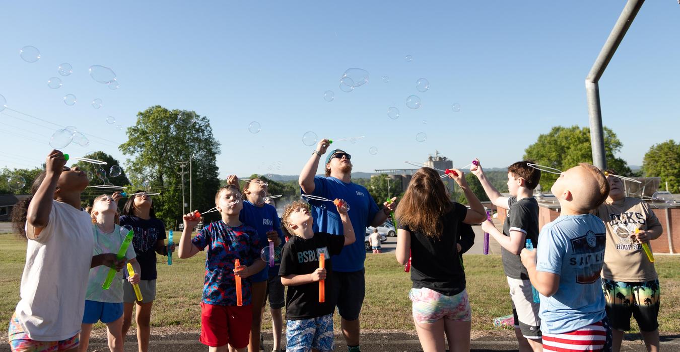 A group of children blowing bubbles outdoors under a clear blue sky.