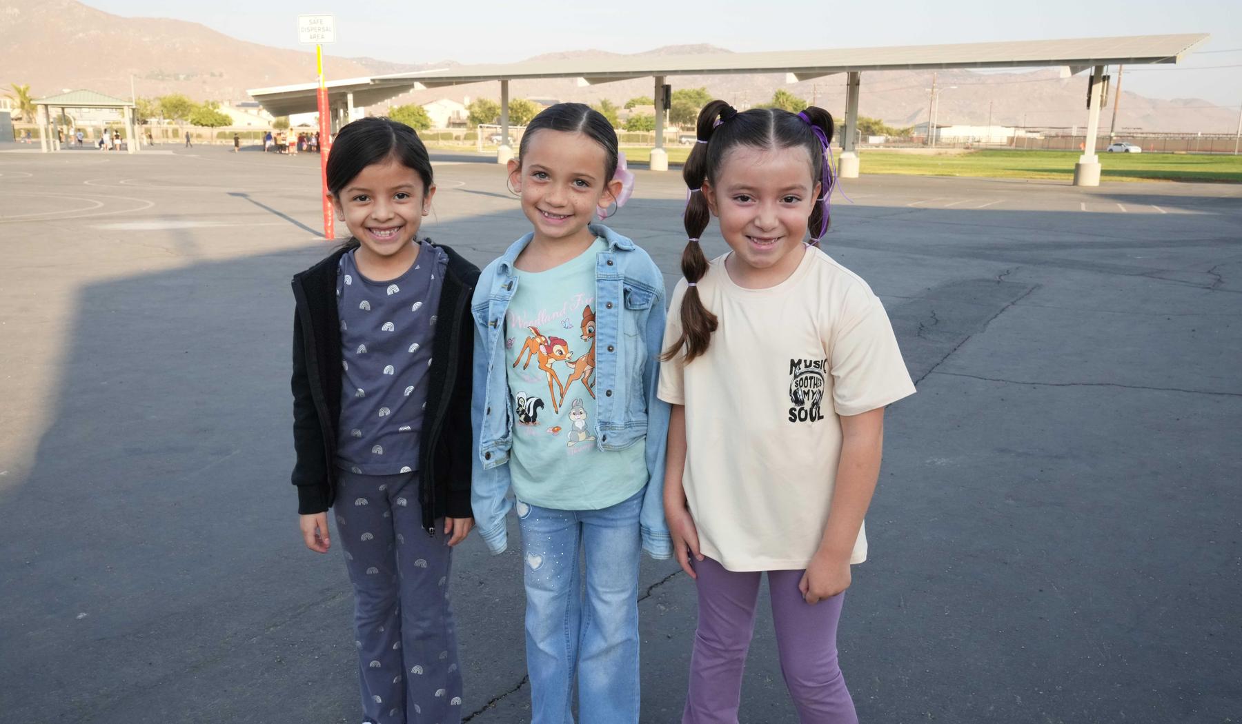 three smiling elementary school girls on blacktop by playground