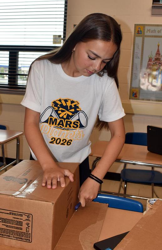 Girl cuts cardboard while working on a project in class.