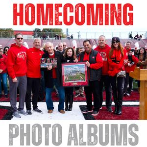 Group of people at a homecoming event holding memorabilia and posing for a photo.